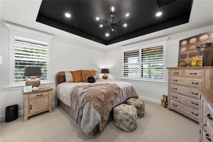Carpeted bedroom featuring a tray ceiling and a chandelier