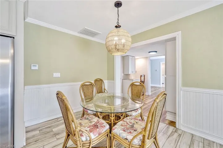 Dining area with a wainscoted wall, an inviting chandelier, visible vents, ornamental molding, and light wood-type flooring