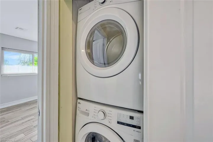Washroom featuring laundry area, light wood finished floors, baseboards, stacked washer and dryer, and visible vents