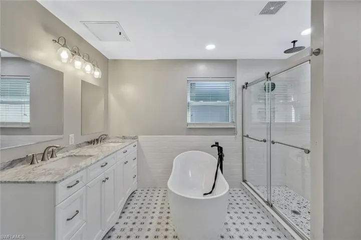 Full bath with a freestanding bath, a sink, visible vents, and a stall shower