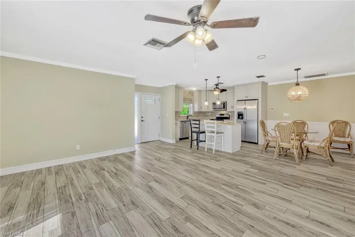 Living room with light wood-type flooring, visible vents, a ceiling fan, and ornamental molding