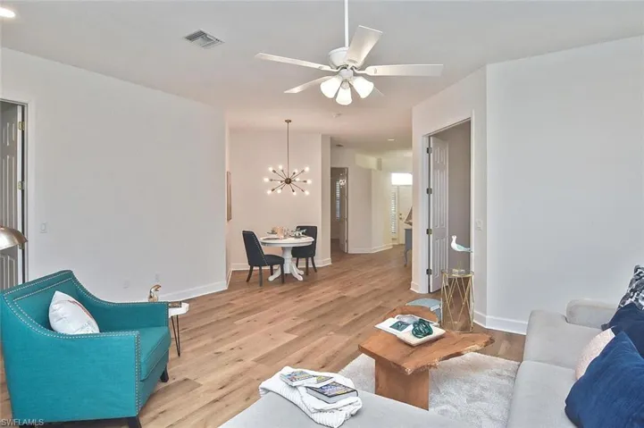 Living room with ceiling fan with notable chandelier and light hardwood / wood-style flooring