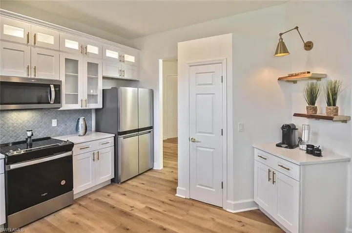 Kitchen with light hardwood / wood-style flooring, stainless steel appliances, tasteful backsplash, white cabinets, and pendant lighting