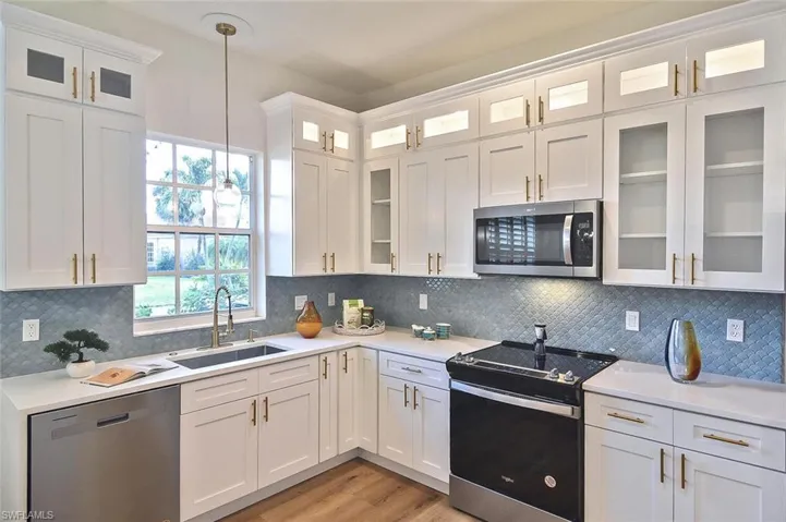 Kitchen featuring light wood-type flooring, backsplash, stainless steel appliances, decorative light fixtures, and sink