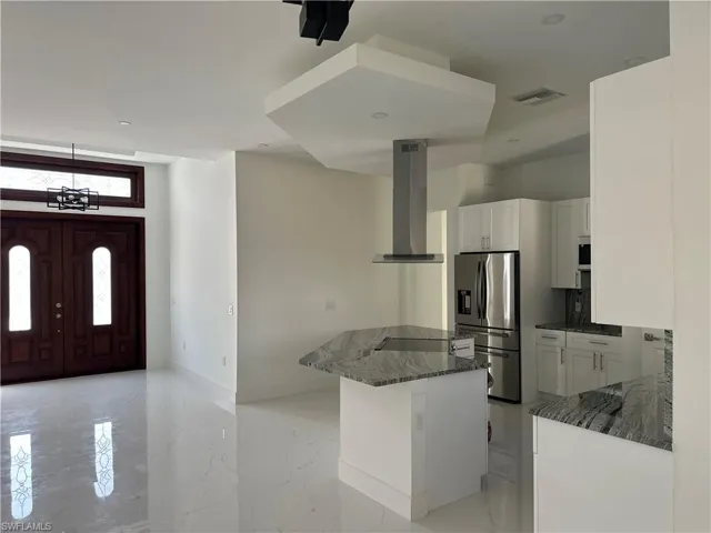 Kitchen featuring dark stone counters, stainless steel fridge, ventilation hood, a kitchen island, and white cabinetry