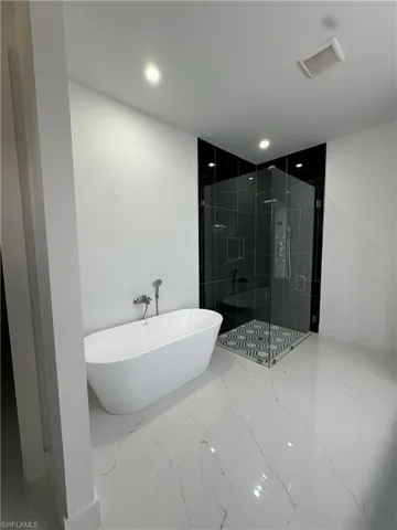 Bathroom with a shower stall, light marble finish flooring, a soaking tub, and recessed lighting