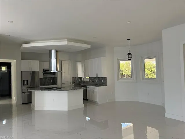 Kitchen with white cabinetry, dark stone counters, stainless steel appliances, range hood, and decorative backsplash