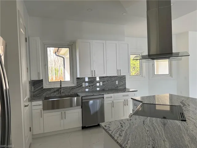 Kitchen featuring island range hood, stainless steel dishwasher, dark stone counters, white cabinetry, and recessed lighting