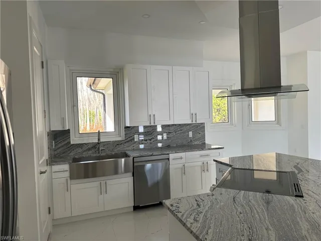 Kitchen featuring dark stone countertops, ventilation hood, white cabinetry, stainless steel appliances, and backsplash