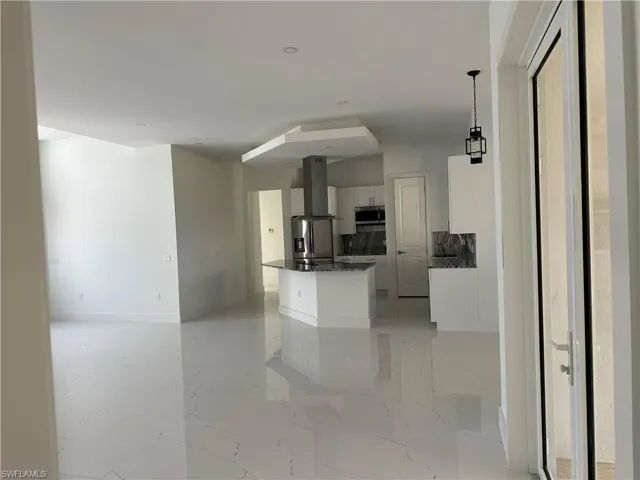 Kitchen featuring white cabinetry, dark stone counters, decorative light fixtures, stainless steel appliances, and light marble finish flooring