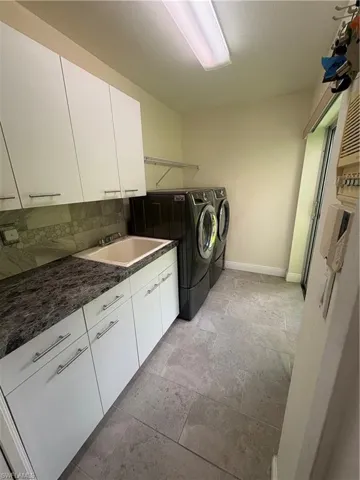Washroom featuring cabinet space, washing machine and clothes dryer, and light stone finish flooring