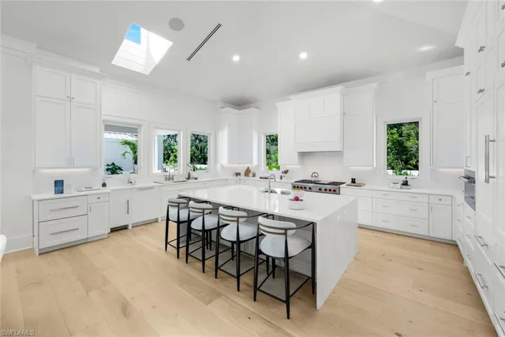 Kitchen with a breakfast bar, an island with sink, light stone countertops, light wood-type flooring, and white cabinetry