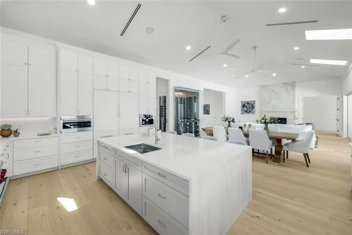 Kitchen with light stone counters, light wood-type flooring, a kitchen island with sink, recessed lighting, and white cabinetry