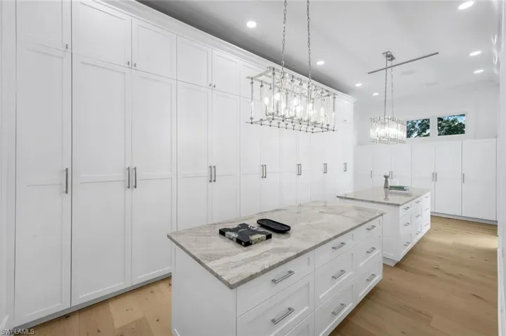 Kitchen featuring light stone counters, light wood finished floors, white cabinetry, hanging light fixtures, and recessed lighting