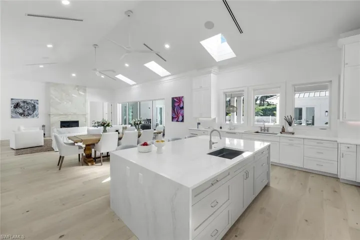 Kitchen featuring white cabinets, light wood-style flooring, a center island with sink, lofted ceiling, and light stone countertops