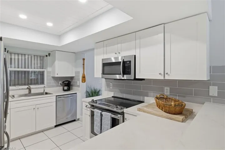 Kitchen with white cabinets, stainless steel appliances, tasteful backsplash, light tile patterned floors, and a raised ceiling