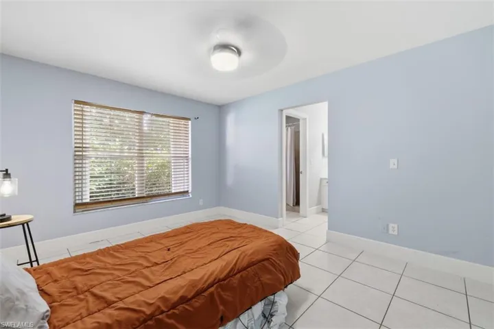 Bedroom with light tile patterned floors, a ceiling fan, and ensuite bath
