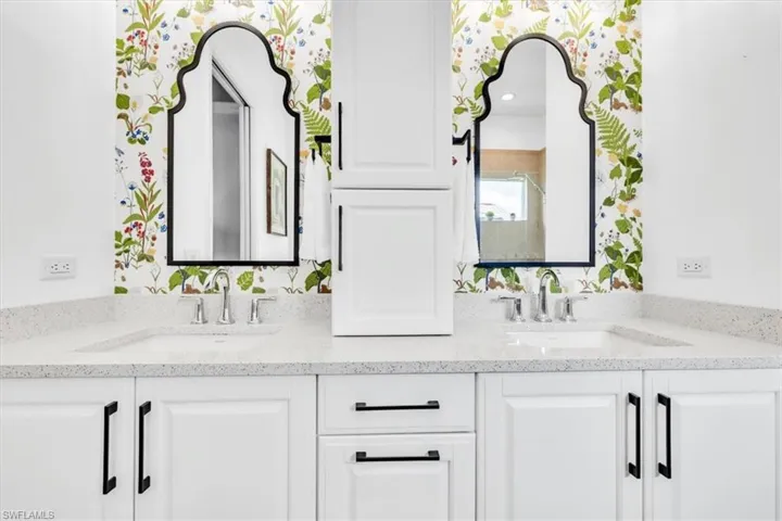 Dual vanity featuring white shaker cabinetry, speckled countertops, chrome fixtures, and ornate black-framed mirrors