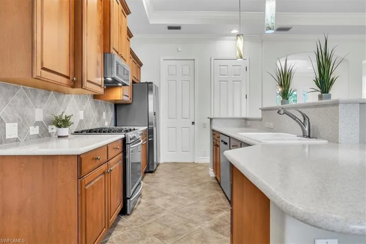 Kitchen featuring wood cabinetry, stainless steel appliances, a tile backsplash, light-toned countertops, and a double basin sink with a gooseneck faucet