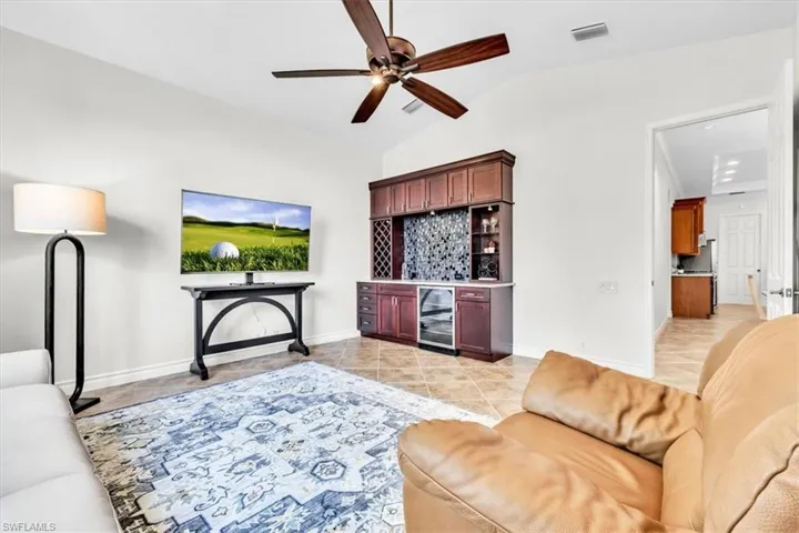 Vaulted ceiling with a ceiling fan, a built-in wet bar with a beverage refrigerator and tile backsplash, and tile flooring