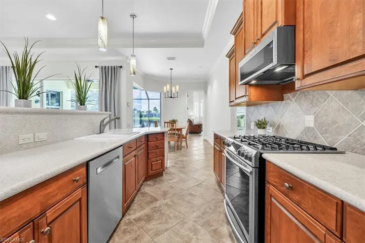 Well-appointed kitchen featuring light-toned countertops, wood cabinetry, stainless steel appliances, and a tile backsplash