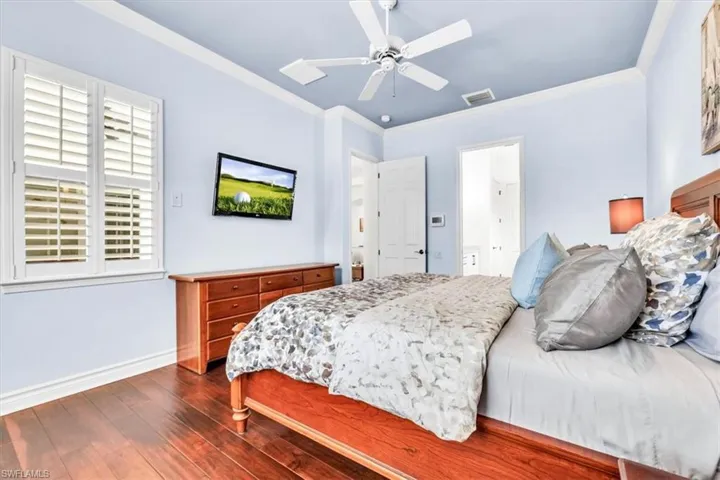 Spacious room featuring wood-finish flooring, white plantation shutters, crown molding, and a ceiling fan