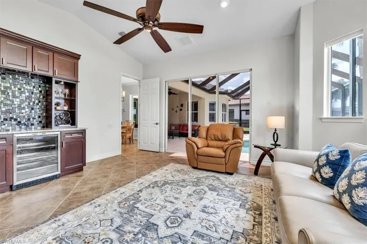 Spacious room featuring vaulted ceilings, a built-in wet bar with a tile mosaic backsplash and beverage cooler, and ceramic tile flooring
