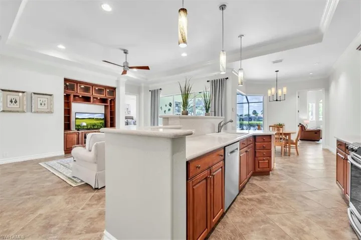 Open concept living area featuring a kitchen island with a double basin sink, light-toned countertops, and wood-finish cabinetry