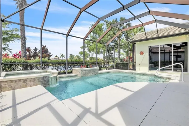 Screened-in outdoor living space featuring a swimming pool, integrated spa with stone tile surround, and a waterfall feature