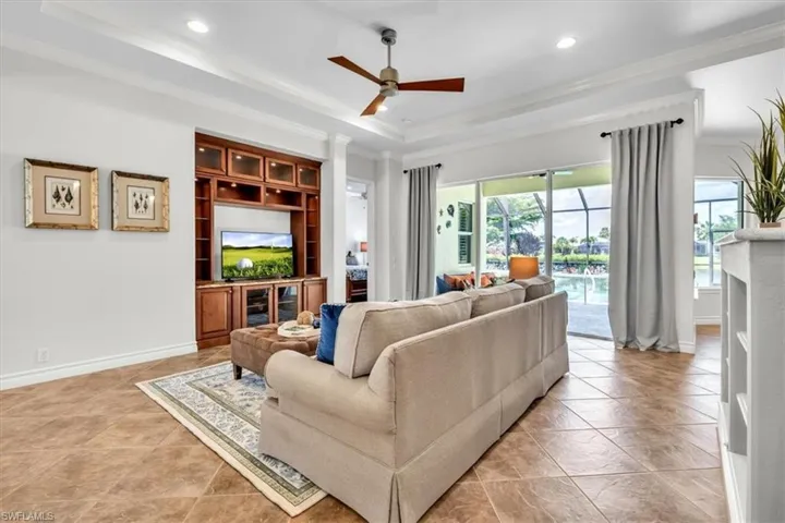 Living area featuring expansive sliding glass doors, built-in entertainment cabinetry with upper glass-front display, crown molding, a ceiling fan, and tiled flooring