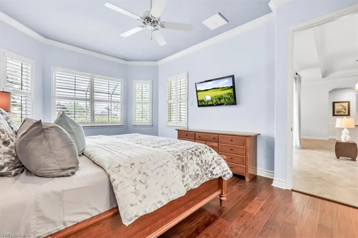 Spacious room featuring wood-finish flooring, a tray ceiling with a ceiling fan, and multiple windows with plantation shutters
