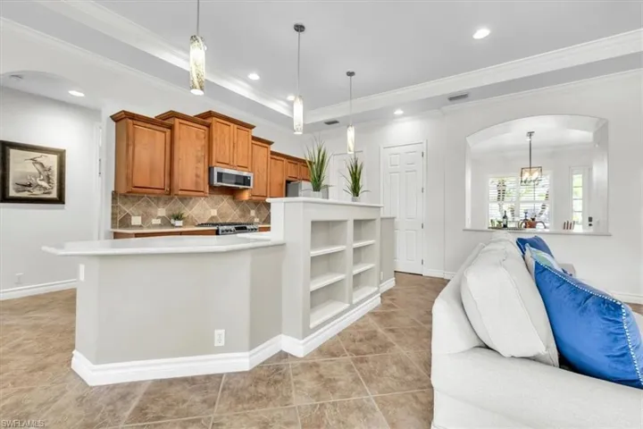 Open-concept kitchen featuring wood cabinetry, stainless steel microwave, tile backsplash, and a breakfast bar with integrated shelving