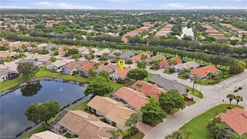 Lakeside property featuring a red tile roof, screened lanai, and mature landscaping within a residential community