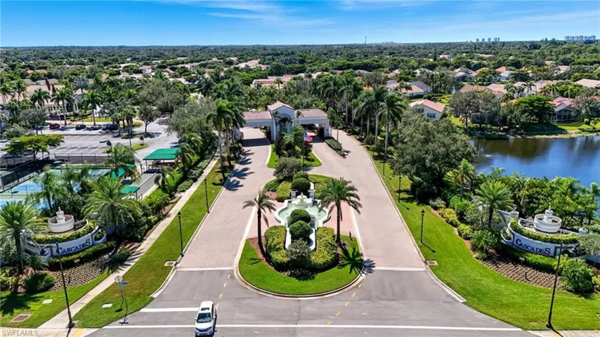 Gated community entrance featuring a decorative fountain, lush landscaping, and mature palm trees