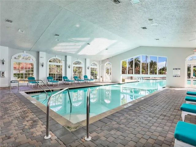 Indoor pool with paver decking, arched windows, and a vaulted ceiling
