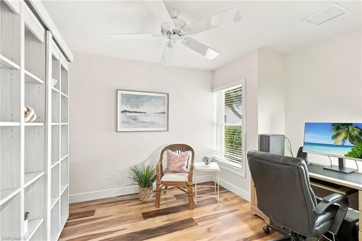 Wood-finish flooring, built-in shelving, white ceiling fan, single window with blinds, and light-toned wall paint