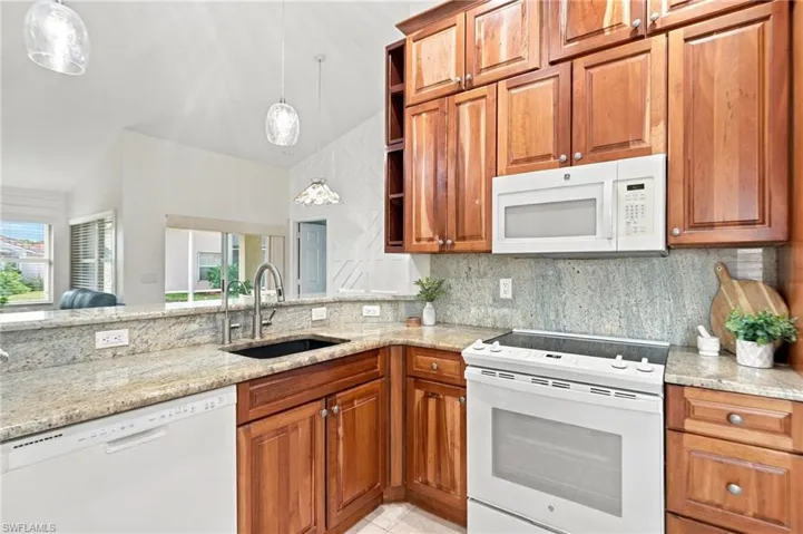 Kitchen featuring abundant wood-finish cabinetry, light-toned granite countertops, and a full suite of white appliances