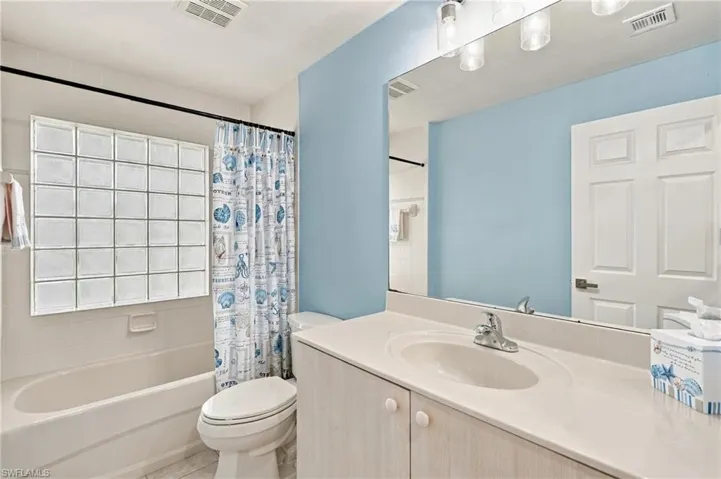 Bathtub with glass block window, single vanity with integrated sink, and large wall-mounted mirror