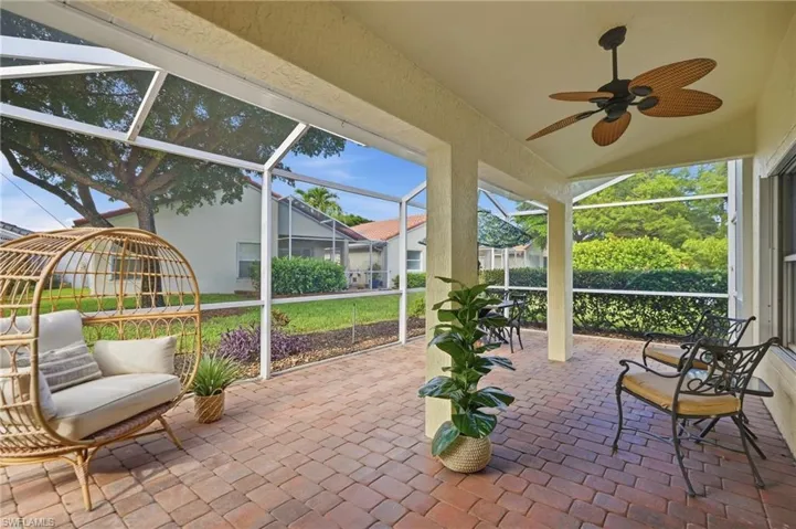 Screened patio featuring a ceiling fan, tiled flooring, structural columns, and a landscaped yard beyond