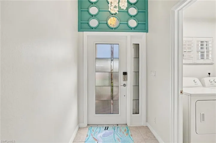 Entry door with decorative glass panels, transom window with accent trim, and tile flooring