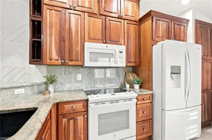 White appliances, wood-finish cabinetry, light-toned countertops, and a tile backsplash