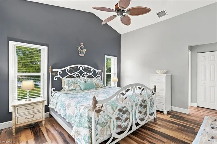 Vaulted ceiling with a ceiling fan, dual windows, wood-finish flooring, and bi-fold closet doors