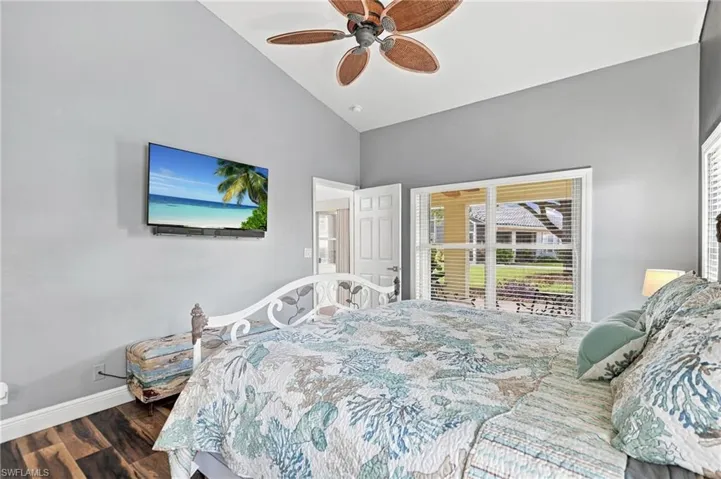 Vaulted ceiling with a ceiling fan, wall-mounted television, wood-finish flooring, and a window with blinds