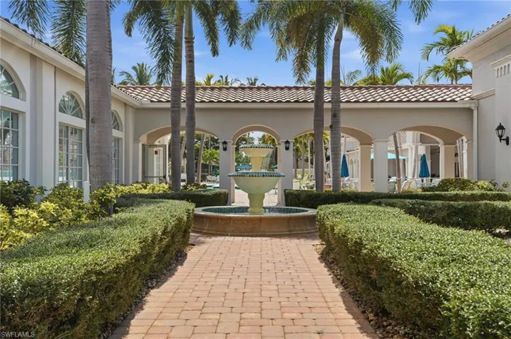 Brick paver pathway with manicured hedges, centered water feature, and arched architectural details