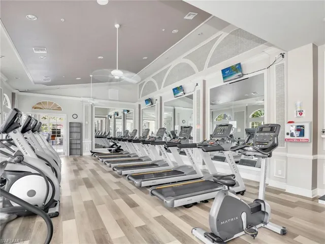 Spacious fitness center featuring wood-finish flooring, vaulted ceilings, and decorative arched windows