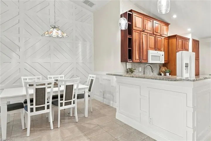 Vaulted ceiling with decorative wall paneling, built-in kitchen cabinetry, and a granite-topped peninsula