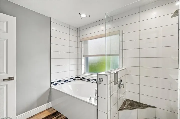 Built-in soaking tub with decorative tile accents, glass-enclosed shower with a built-in bench, and wood-finish flooring