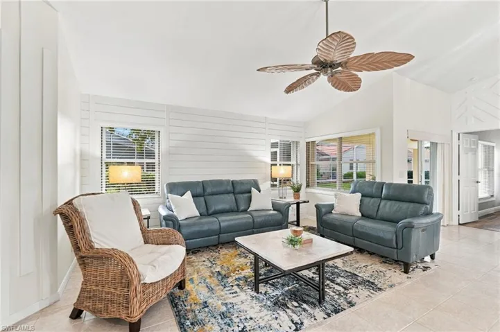 Vaulted ceilings with a decorative ceiling fan, horizontal plank wall accents, multiple windows with blinds, and tile flooring