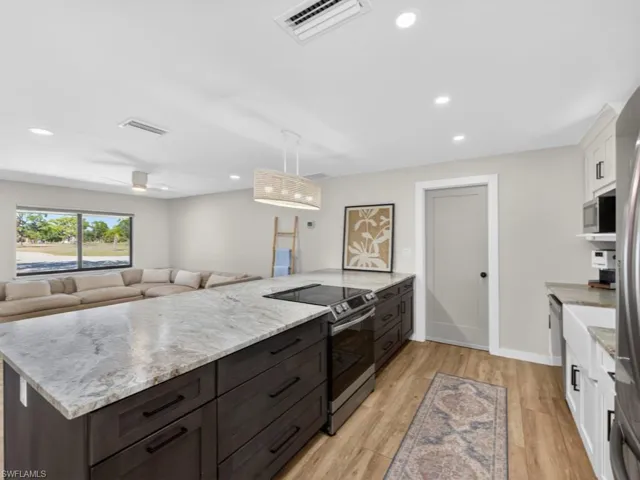 Kitchen featuring stainless steel appliances, white cabinets, light stone counters, hanging light fixtures, and light wood-type flooring
