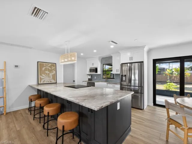 Kitchen featuring leatherwood granite  counters, a kitchen bar, black appliances, white cabinets, and recessed lighting